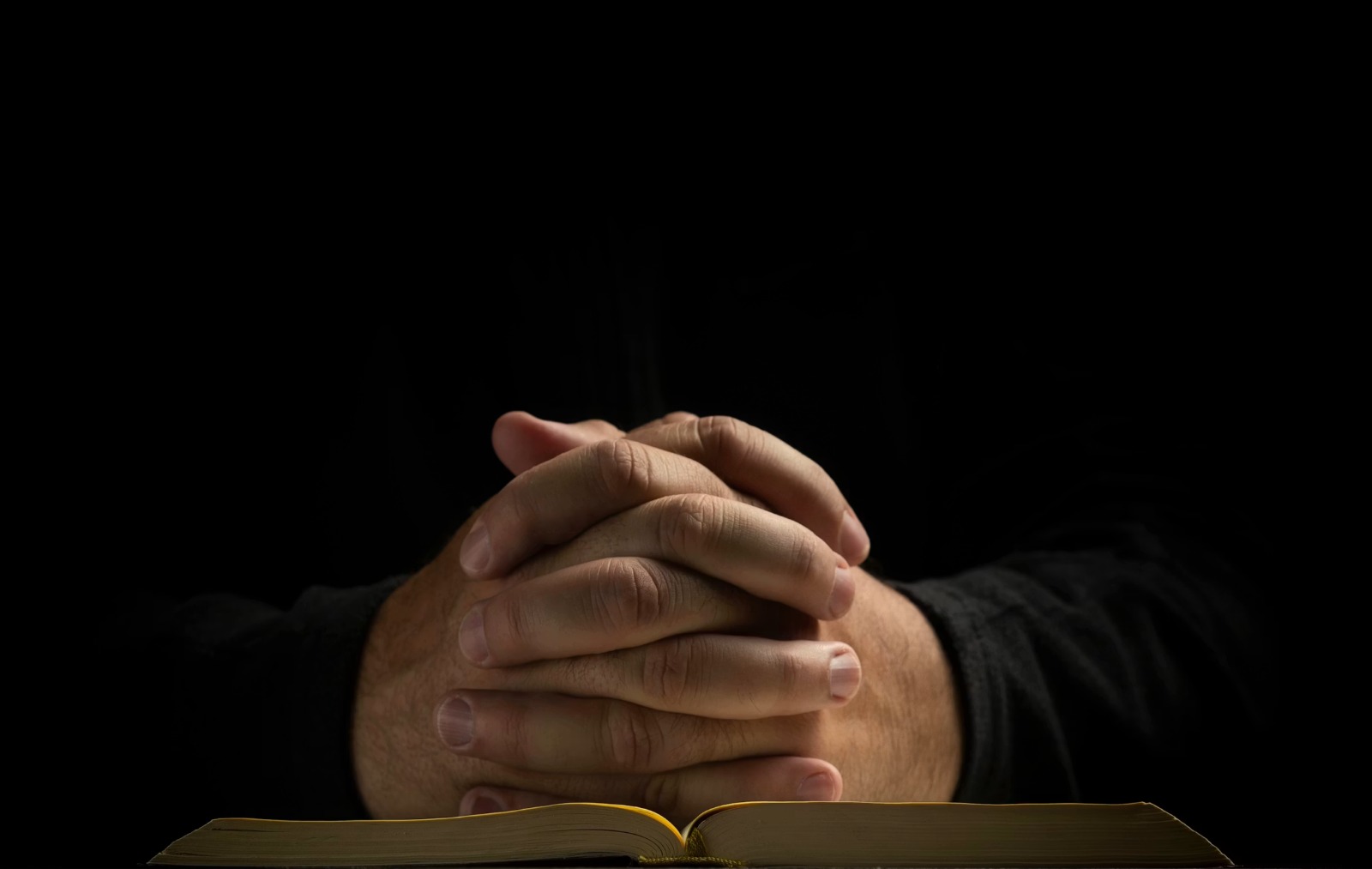 Hands clasped in prayer over an open Bible